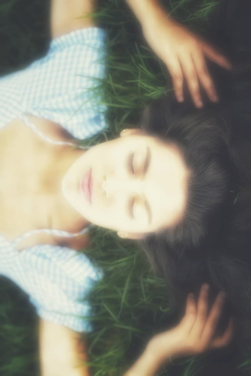 A young woman lying in the grass with her eyes closed, resting in warm sunlight.